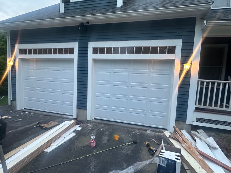 Completed dual white garage doors with transom windows on blue colonial at dusk